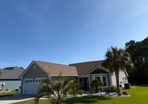 Suburban single-story house with a tan roof, white columns, palm trees, and a bright blue sky