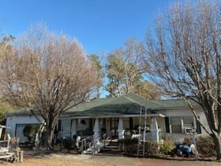 A single-story white house with a green roof, porch, and bare trees on a sunny day.