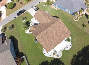 Aerial view of a suburban house with a tan roof, green lawn, driveway, and neighboring homes.