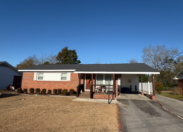 Brick ranch house with carport and driveway, clear blue sky.