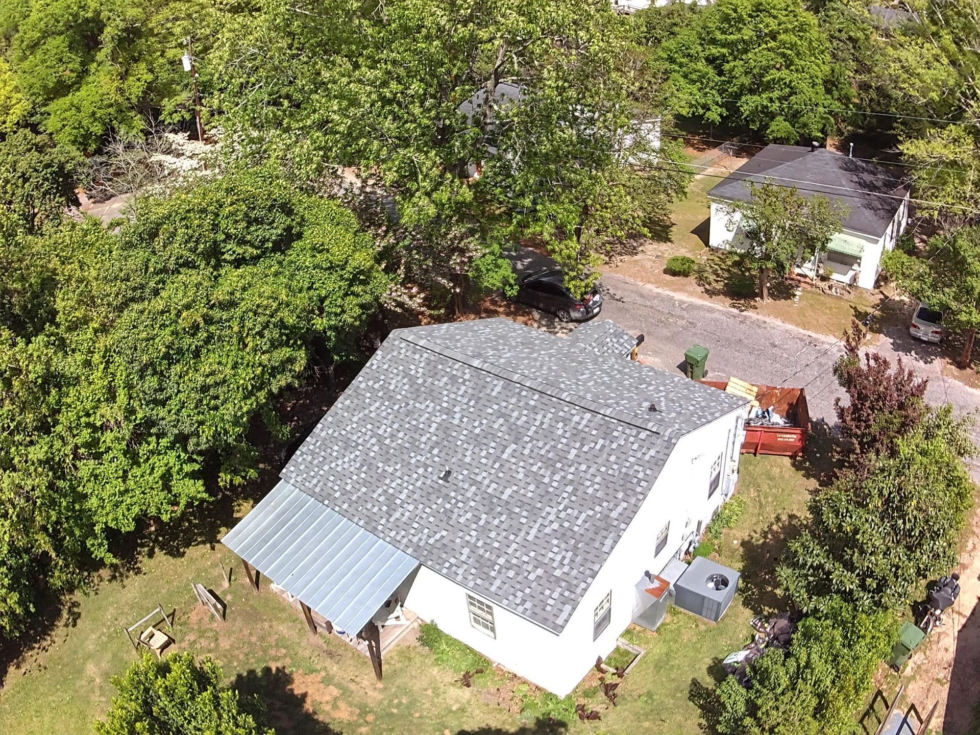 Aerial view of a white house with a gray roof, surrounded by trees and a grassy yard