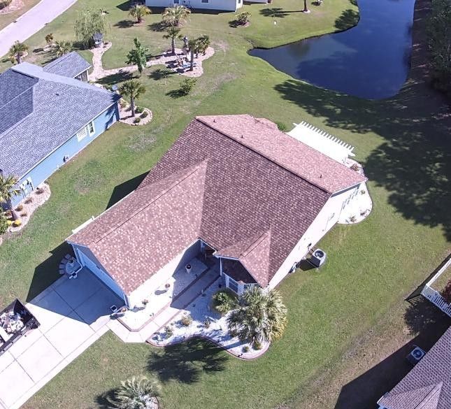 Aerial view of a suburban house with a red roof, driveway, lawn, and a pond nearby.
