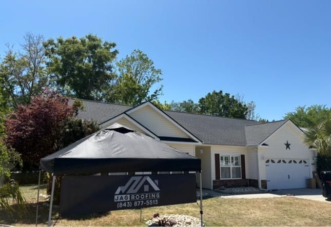 House with a black tent and construction sign in the front yard, under a clear blue sky