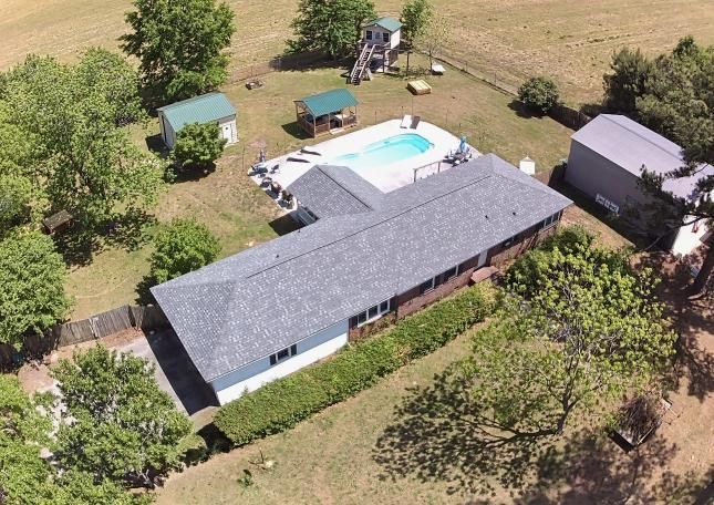 Aerial view of a house with a backyard pool, patio, and surrounding trees and lawn