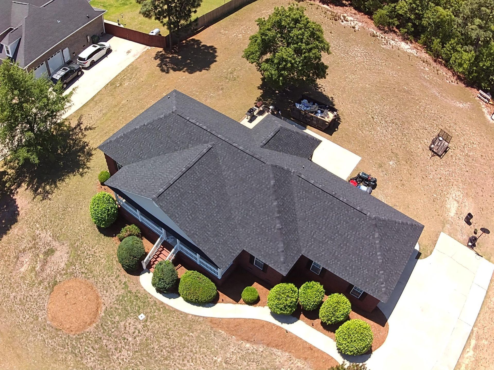 Aerial view of a dark gray-roofed house with a tan yard and trees around it.