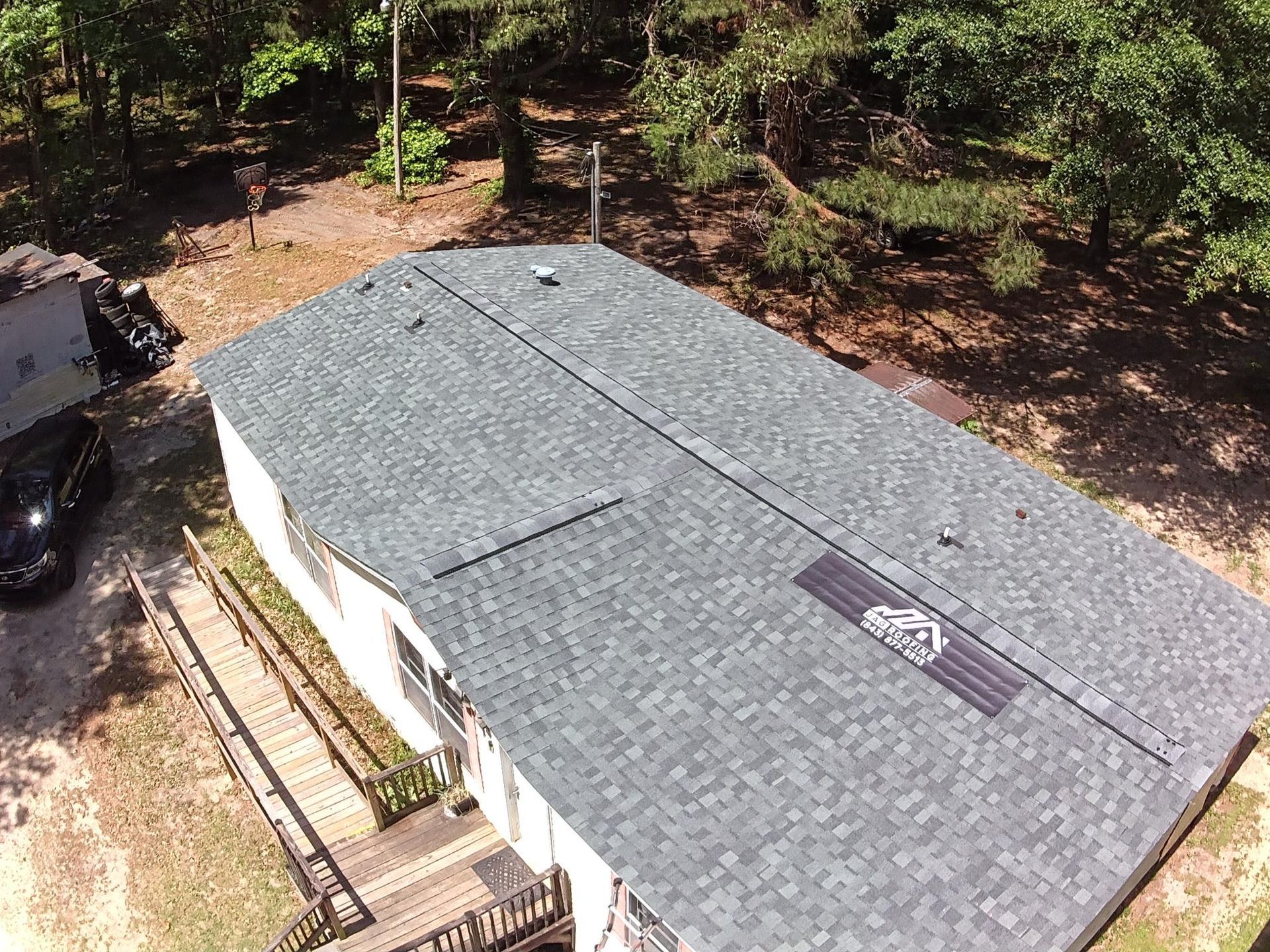 Aerial view of a gray shingled house roof with trees and a driveway beside it