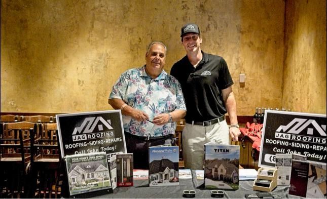 Two men behind a display table at an indoor trade show, smiling with promotional signs and products.