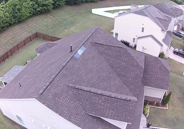 Aerial view of a gray-shingled house roof in a suburban backyard.