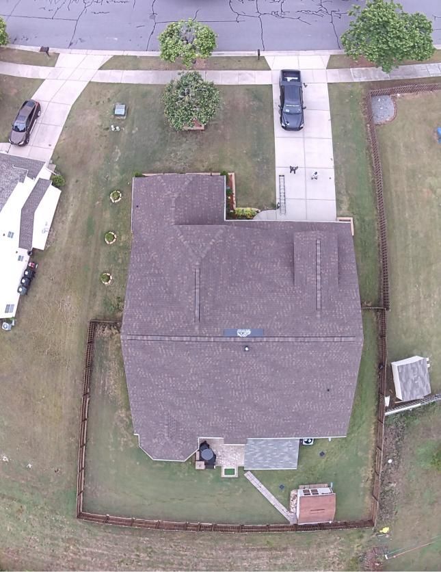 Aerial view of a house with a large yard, driveway, and parked vehicles on a residential street.