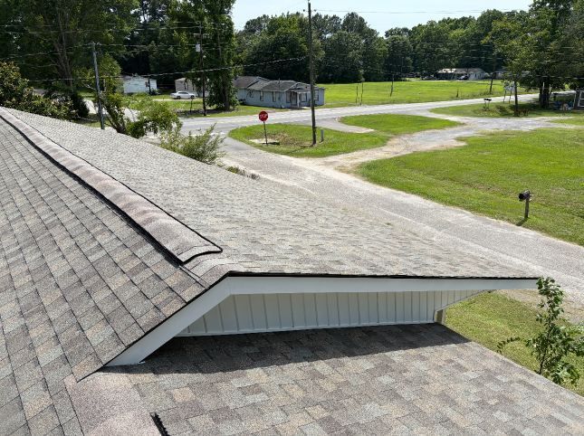Rooftop with gray shingles overlooking a grassy park and road intersection under clear skies