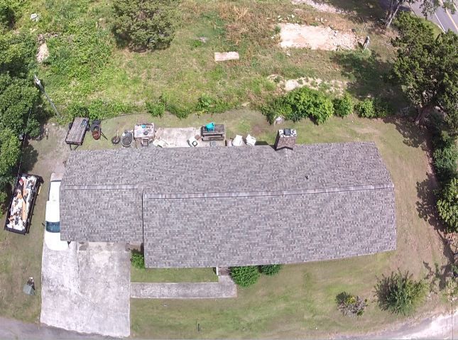Aerial view of a long gray-roofed house with a small porch, surrounded by grass and trees.
