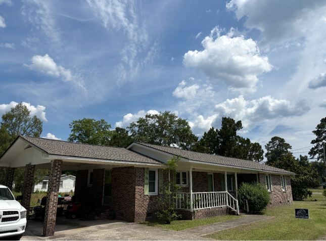 Single-story brick house with a screened porch, white railing, and cloudy blue sky above