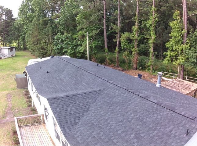 Black shingled roof with trees and a grassy yard in the background