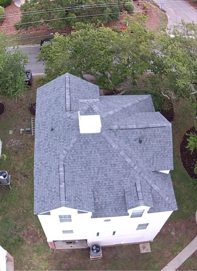 Aerial view of a white two-story house with a gray roof surrounded by trees and a sidewalk.