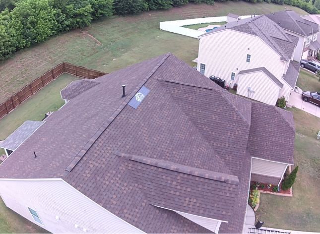 Aerial view of a suburban house with a gray roof, backyard, and neighboring homes.
