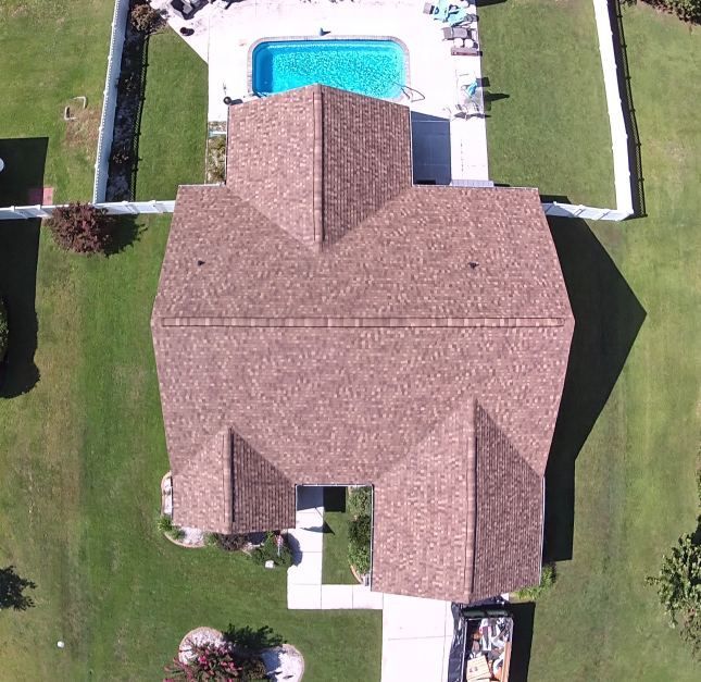 Aerial view of a house with a brown roof, backyard pool, and green lawn.