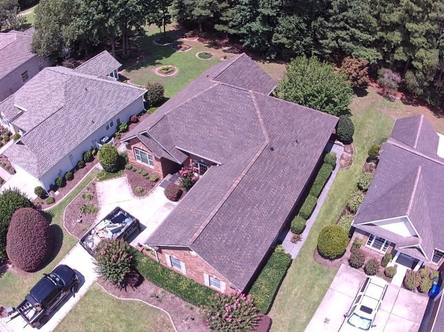 Aerial view of suburban houses with driveways, lawns, and trees in a residential neighborhood.