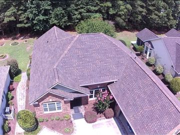 Brown shingled roof with a chimney and open skylight against a blue sky.