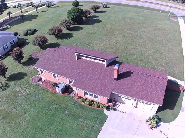 Aerial view of a brick house with a red roof, white garage, and large grassy yard.