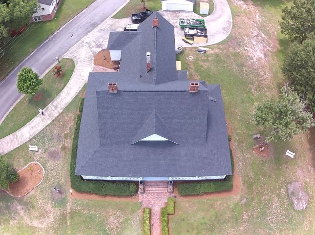 Aerial view of a house with a dark roof, driveway, and surrounding lawn.