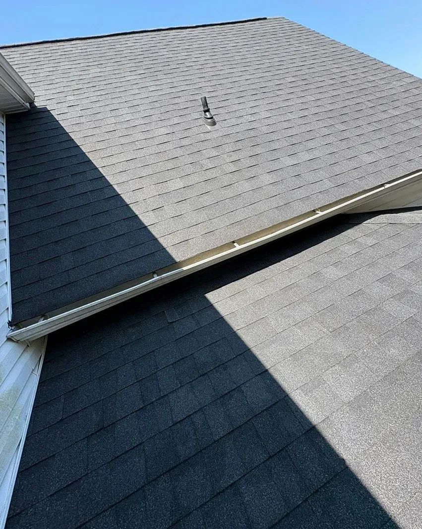 A close-up of a roof showing shingles in shades of gray, casting a diagonal shadow.