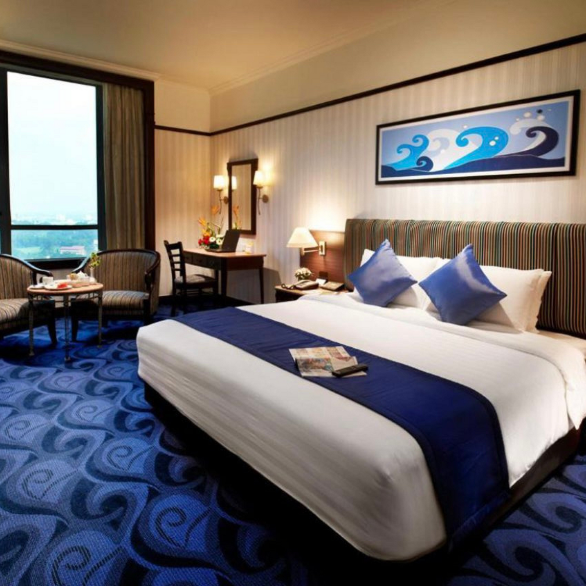 Hotel room with a large bed, blue patterned carpet, desk, and a view through a window.