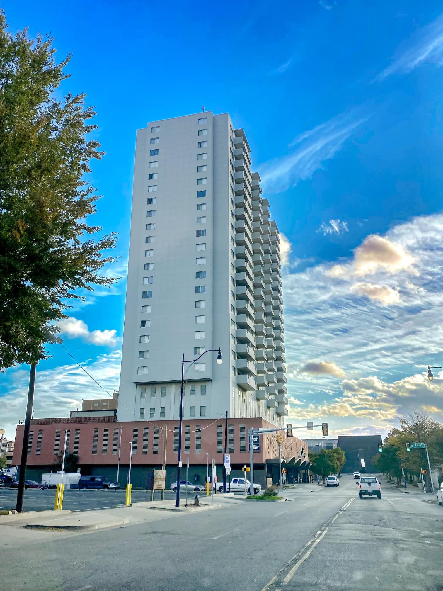 Tall white apartment building on a city street under a partly cloudy blue sky.