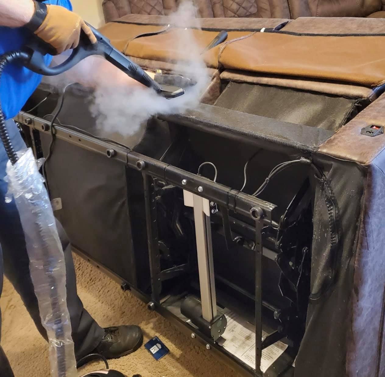 Person steam cleaning the interior mechanism of a brown recliner couch. Steam is released.