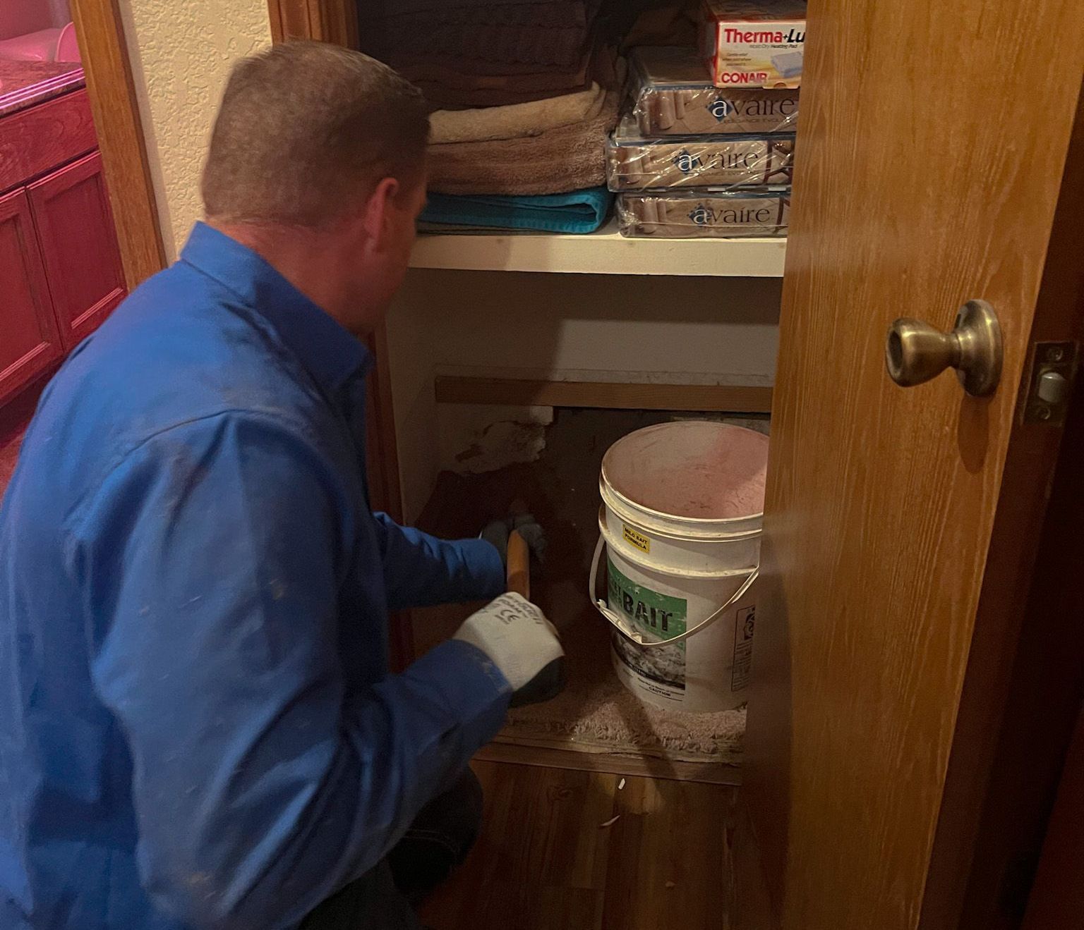Man in blue shirt works in a closet, using a tool. A bucket is on the floor.