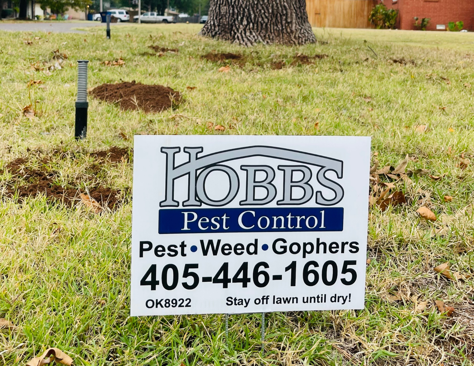 Sign for Hobbs Pest Control, targeting pests, weeds, and gophers, in a grassy yard. Phone number included.