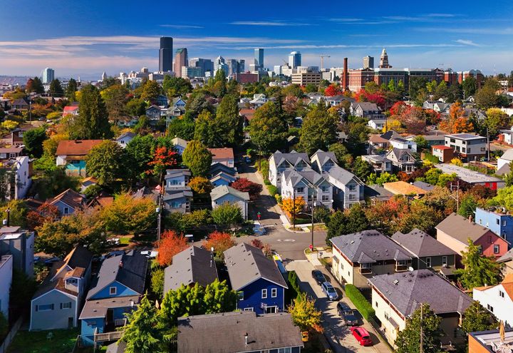 Aerial view of colorful houses and trees with a city skyline under a blue sky.