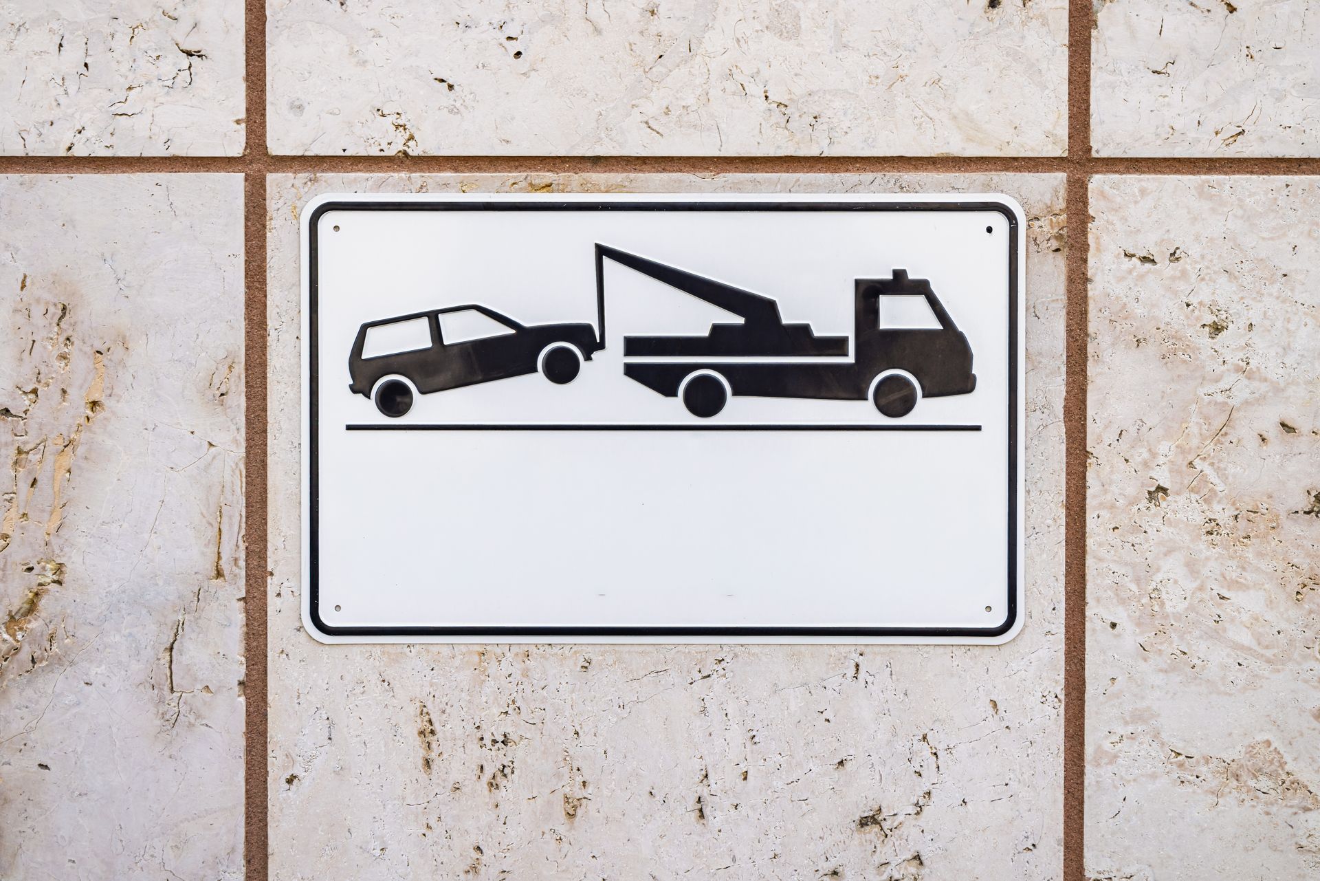 Tow truck loading a small car on a wall-mounted parking sign plaque.