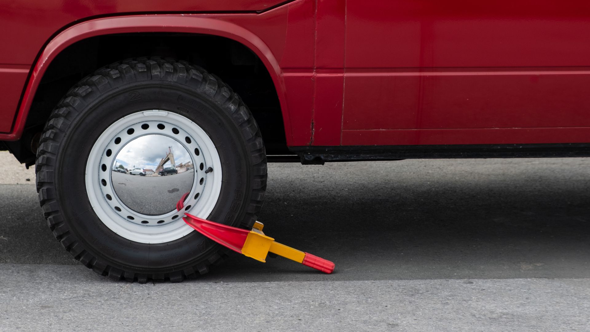 Red vehicle wheel secured with a wheel clamp to prevent unauthorized movement.