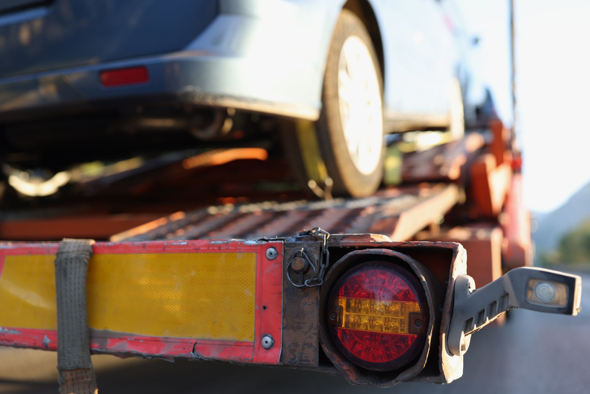 Close up of a red car lifted by a tow truck with the front wheel secured by lifting gear.