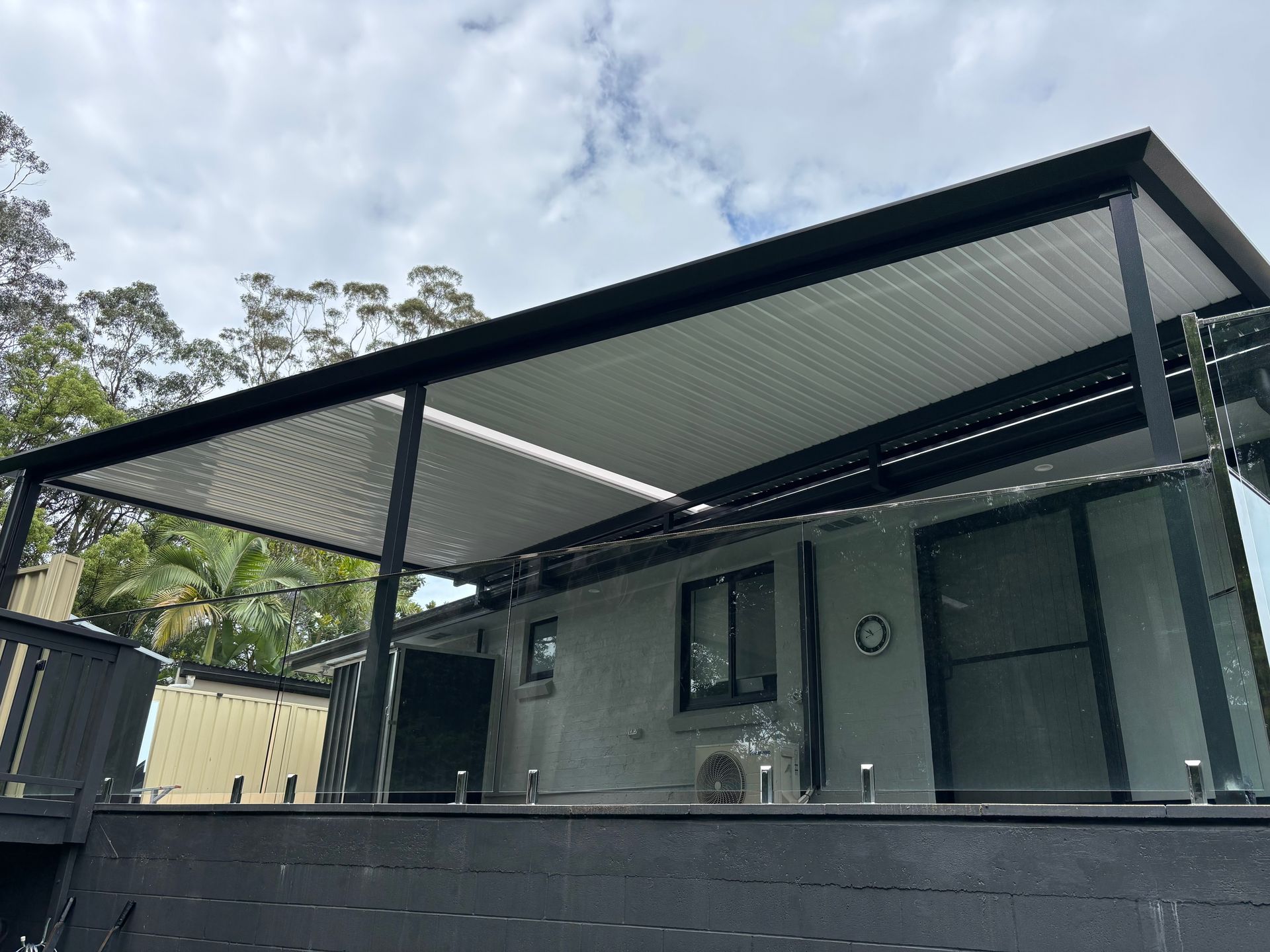 Black-framed Patio Cover Over a Gray Building With Glass Railings — In The Central Coast