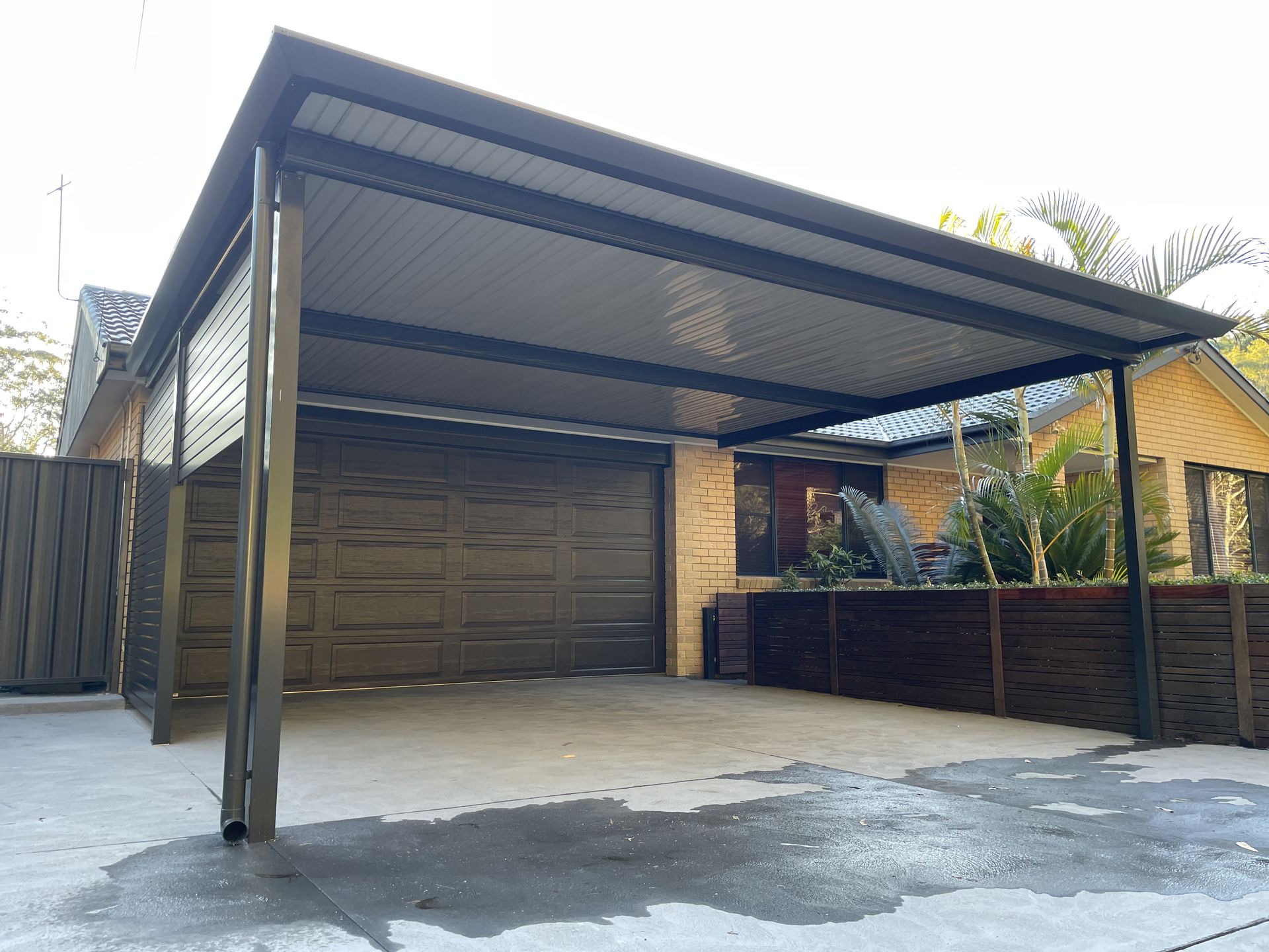 A car is parked under a canopy in a driveway. — Outdoor Leisure Living In Tuggerah, NSW