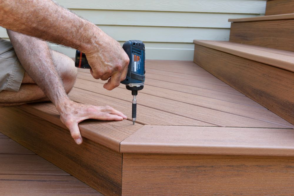 A Man is Using a Drill on a Wooden Deck — Outdoor Leisure Living In Bateau Bay, NSW