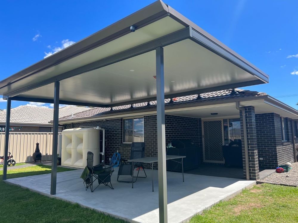 A Patio With a Table and Chairs Under a Canopy in Front of a House — Outdoor Leisure Living In Woy Woy, NSW 
