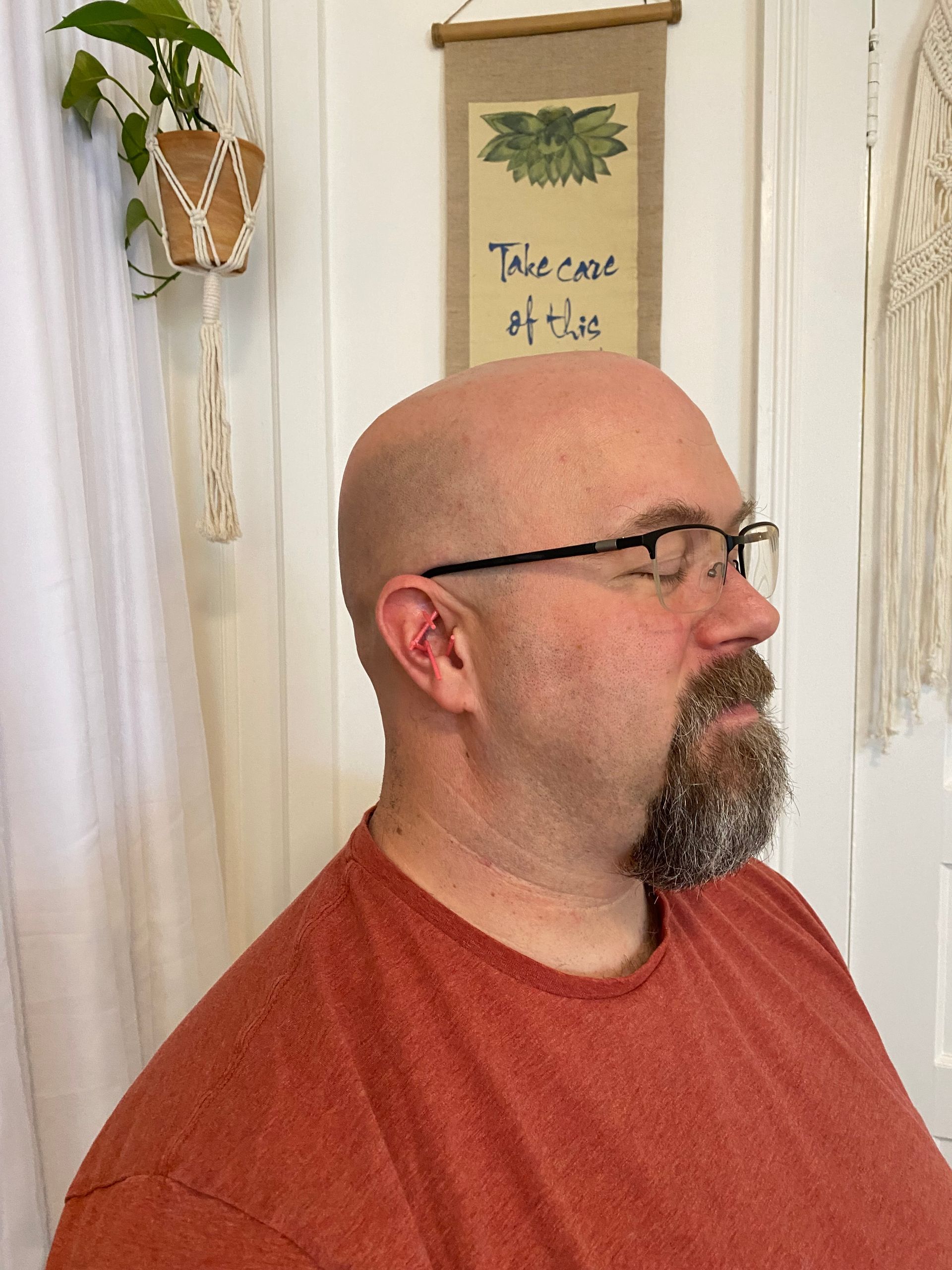 A man with glasses and a beard is wearing an orange shirt.
