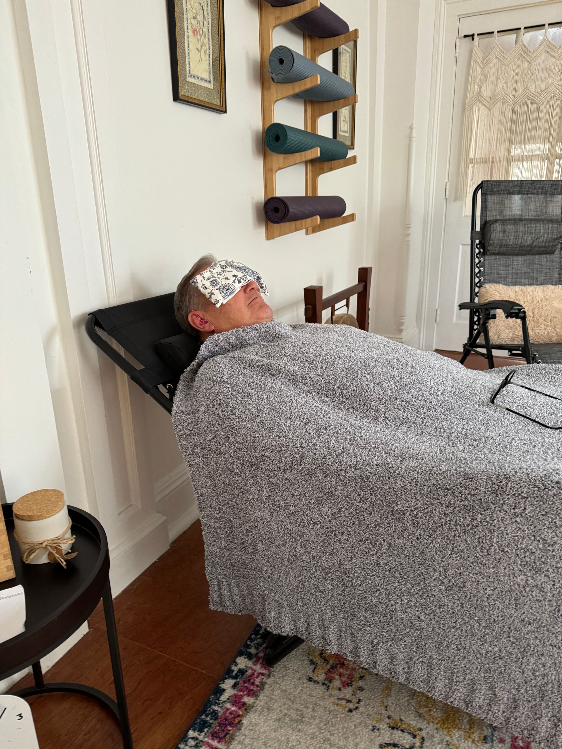 A man is laying on a bed with a blanket on his head.