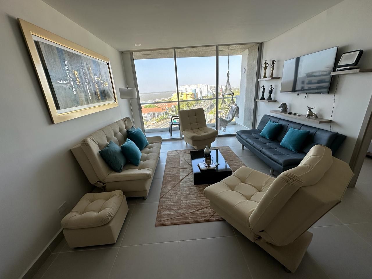 Sala de estar con muebles beige, cojines azules y vista a la ciudad.  | Mevak Agency