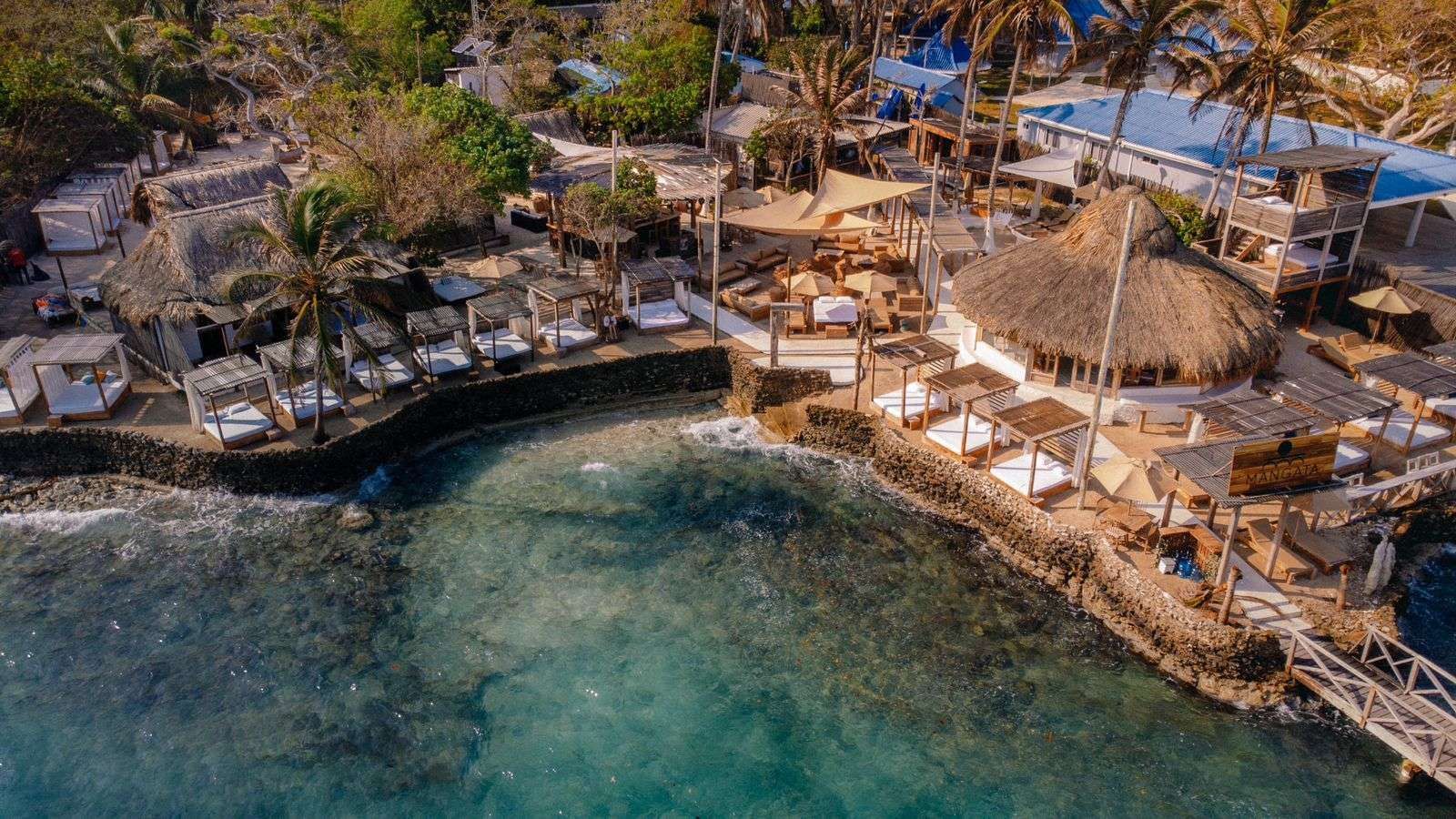 Vista aérea de un complejo turístico junto a la playa con estructuras con techo de paja,  | Mevak Agency