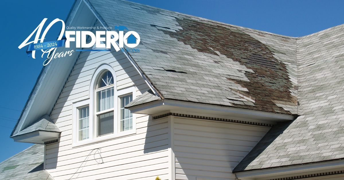 White house roof with heavy shingle damage, showing missing and curled shingles near a dormer window.
