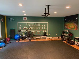 Home gym with baseball theme, green walls, equipment, Fenway Park scoreboard, baseball stadium photo.