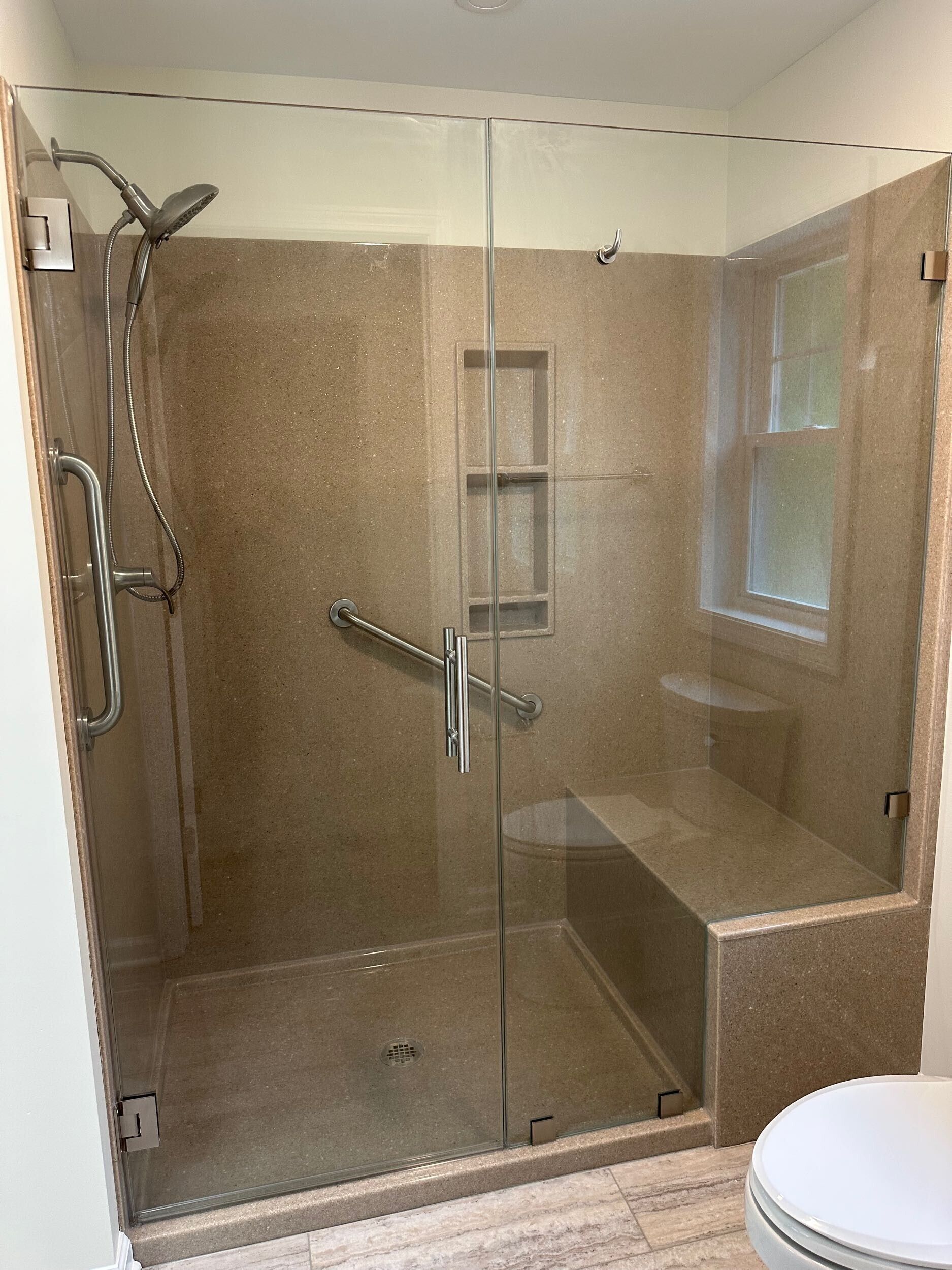 Glass shower with bench and built-in niche. Beige tile walls. Chrome fixtures. Toilet visible.