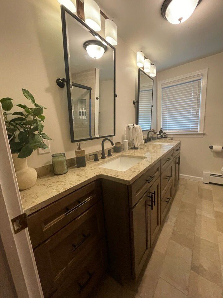 Bathroom with double sinks, brown cabinets, beige countertop, mirrors, and window with blinds.