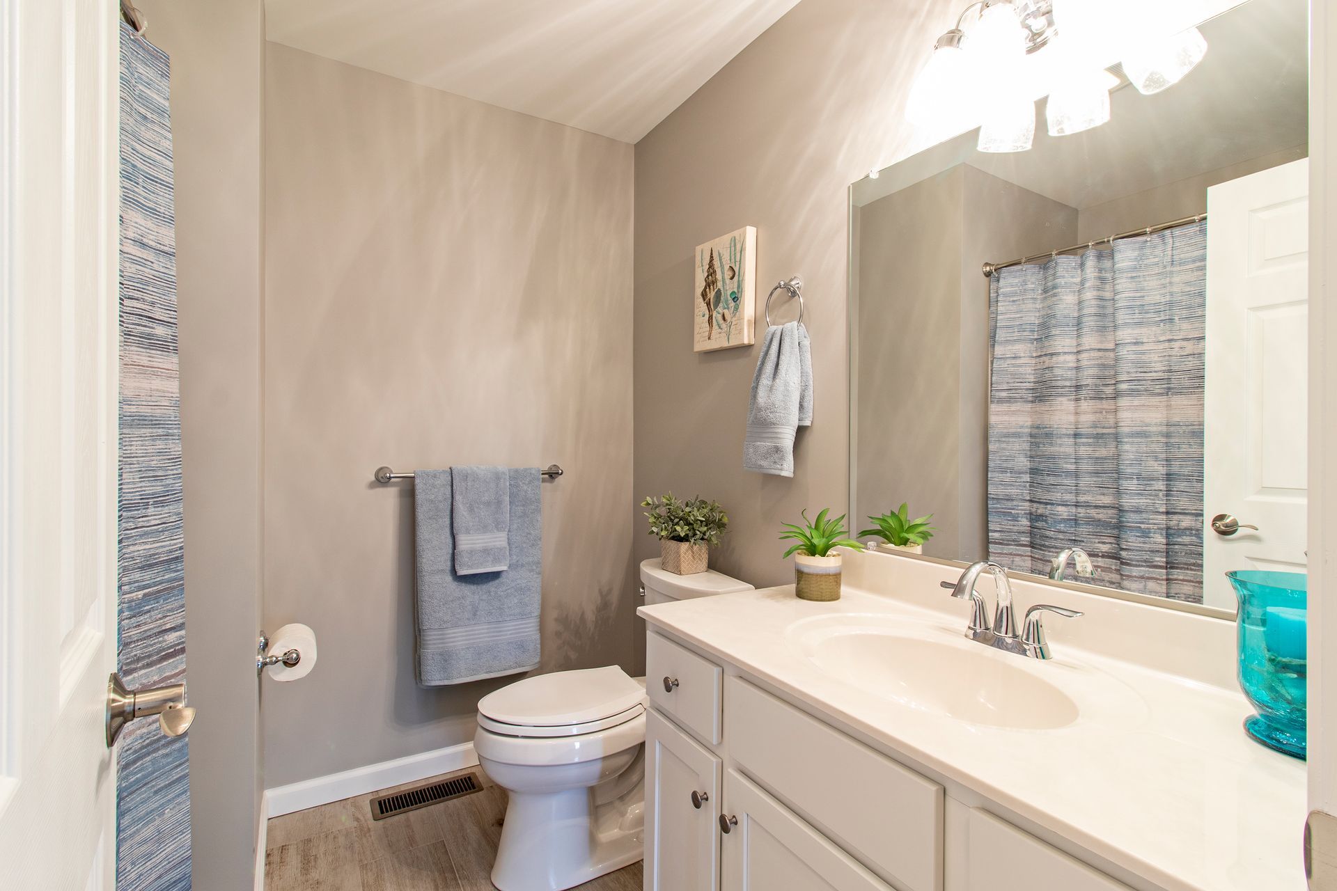Bathroom with gray walls, white vanity, toilet, mirror, and blue shower curtain.