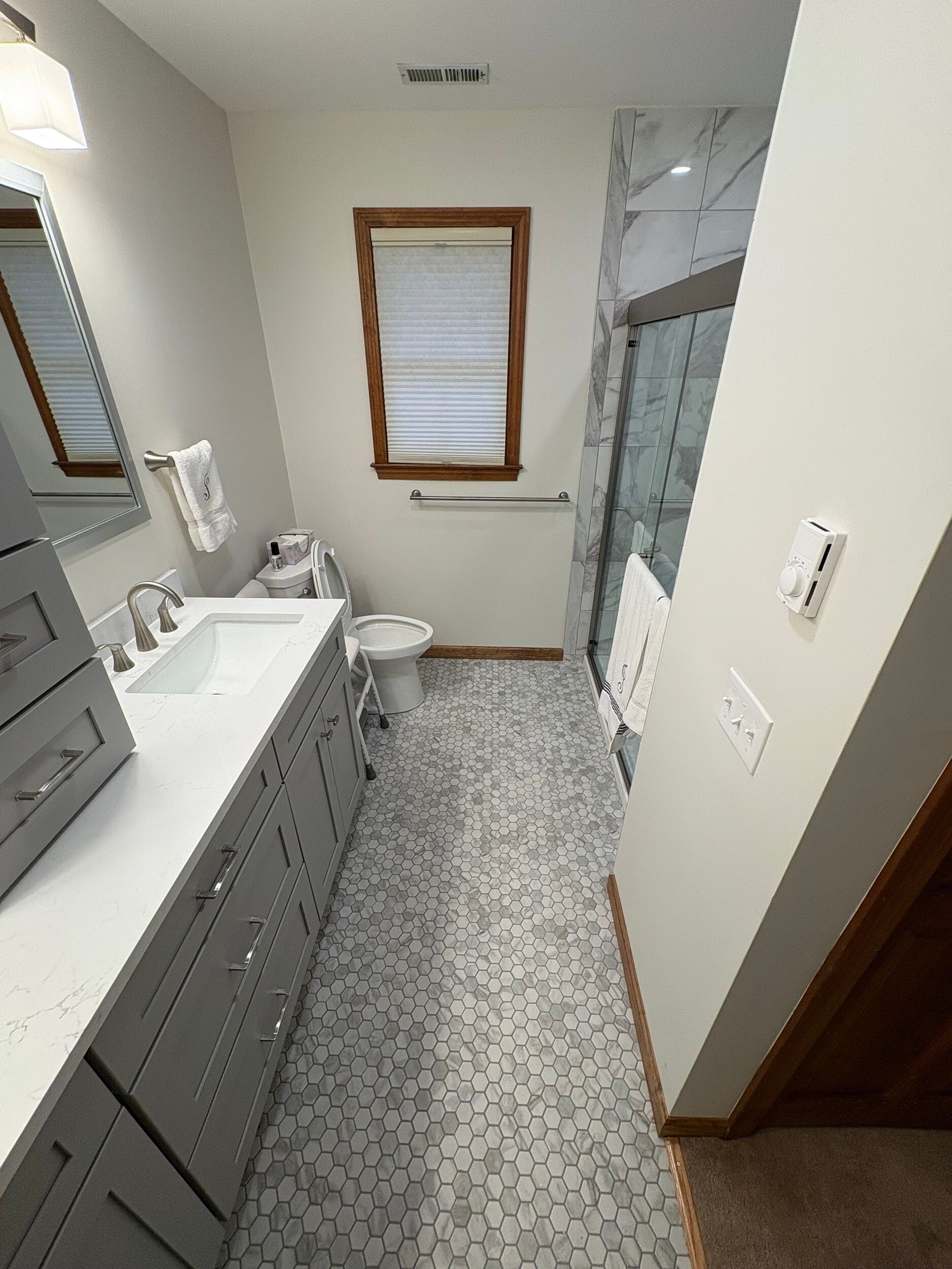Bathroom with gray vanity, patterned floor tiles, white walls, and a glass shower.