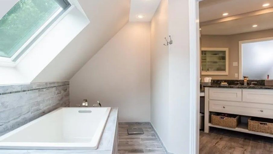 Bathroom with bathtub under sloped ceiling; adjacent to vanity with open doorway.