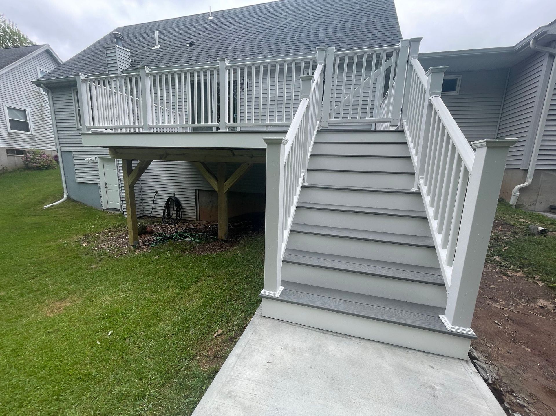 Gray deck with stairs and white railing on a house, viewed from the lawn.